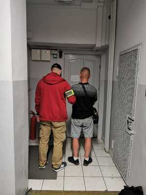 sprawca rozboje stojący tyłem obok stoi policjant, który trzyma go pod rękę