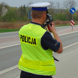 policjant stoi na poboczu jezdni i mierzy prędkość nadjeżdzającym pojazdom