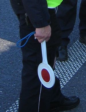 stojący policjant trzyma w ręcę tarcze służacą do zatrzymywania pojazdów