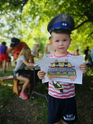 Chłopiec w czapce policyjnej trzymający pokolorowany obrazek – radiowóz.