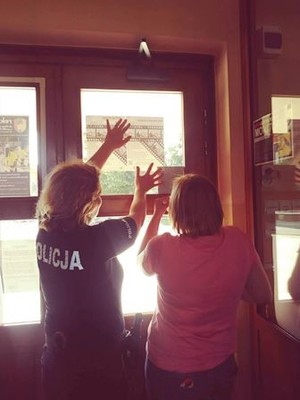funkcjonariuszka wraz z kobieta przyklejają plakat na oknie