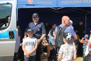policjant pozuje do zdjęcia z dziewczynką przy radiowozie, w tle stoisko profilaktyczne