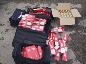 cztery torby bagażowe otwarte, wypełnione wagonami papierosów, a obok otwarty karton z butelkami z cieczą