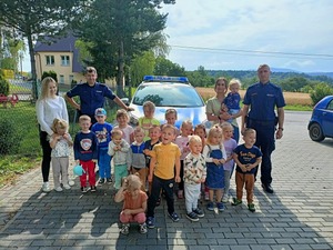 Umundurowani policjanci oraz dzieci stojące przed radiowozem policyjnym