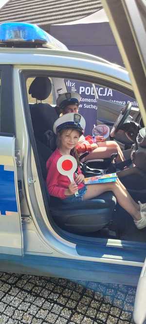 dziewczynka siedząca w radiowozie  z czapką policyjna i tarczą