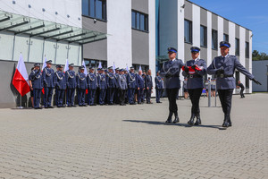 Trzech policjantów maszerujących ze złożoną flagą w stronę masztu