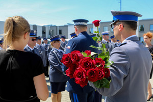 Policjant trzyma czerwone róże dla policjantek, które otrzymały odznaczenia