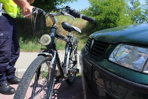 Rower stojący przed maską zielonego volkswagena. Policjant sprawdza ułożenie śladów na obu pojazdach.