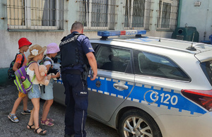 policjant pokazuje dzieciom radiowóz na parkingu przy komisariacie