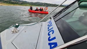 Na zdjęciu widać fragment policyjnej łodzi , a dalej motorową łódź strażacką na której płynie trzech strażaków i policjant.