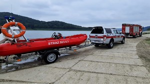 Wóz strażacki oraz oznakowany samochód Straży Pożąrnej z pryczepą, na której jest łódź