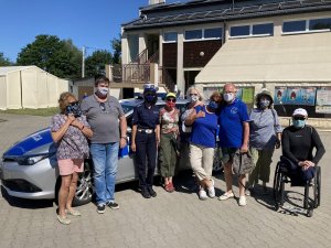 seniorzy z policjantką na tle radiowozu przed budynkiem