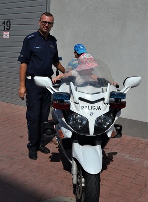 dwójka małych dzieci siedzi na policyjnym motocyklu, obok stoi policjant