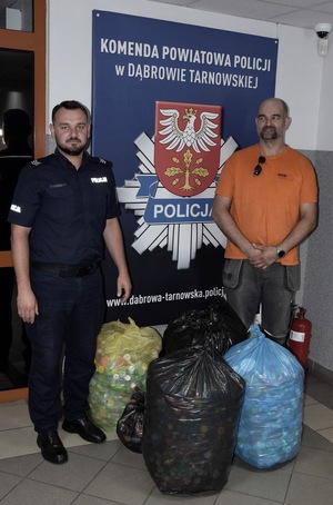 policjant i mężczyzna ubrany po cywilnemu stoją z workami wypełnionymi zakrętkami