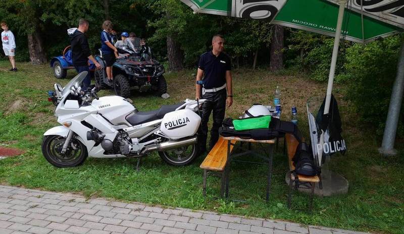 umundurowany policjant na stoisku policyjnym, obok oznakowany motocykl, w tle quad