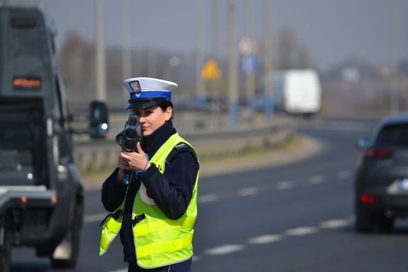 Policjantka ruchu drogowego trzyma w ręku ręczny miernik prędkości. Nadzoruje ruch na drogach
