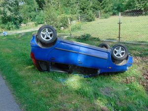 niebieskie auto leżące na dachu w rowie