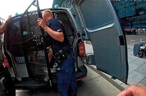 policjant umieszczający zatrzymanego w z tyłu radiowozu podczas zamykania klapy drzwi