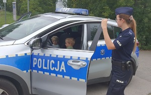 dzieci siedzące w radiowozie obok stoi policjantka