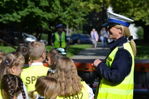 grupka dzieci w kamizelkach odblaskowych z napisem SP92 rozmawia z policjantką ruchu drogowego