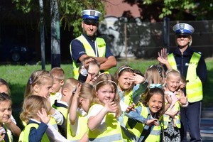 Uśmiechnięte dzieci ubrane w kamizelki odblaskowe pozują do zdjęcia z policjantami ruxhu drogowego przy przejściu dla pieszych