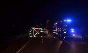 miejsce wypadku drogowego, zmrok, z prawej strony pojazd straży pożarnej, strażacy na ulicy oraz parawan