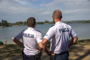 dwóch policjantów komisariatu wodnego w białych, policyjnych koszulkach patrzą na jezioro