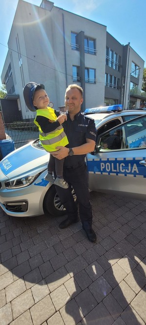 policjant trzyma chłopca w kamizelce odblaskowej na rękach