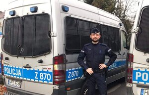 Umundurowany policjant stojący obok radiowozu policyjnego.