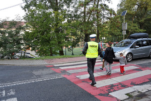 policjant przeprowadzajacy ucznia i osobe dorosłą przez przejście dla pieszych