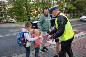 policjant wręczający opaski odblaskowe dzieciom