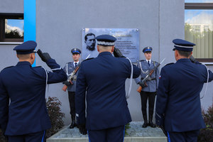 Delegacja z komendantem wojewódzkim salutuje pod tablicą Ludwika Drożańskiego. Widok zza pleców