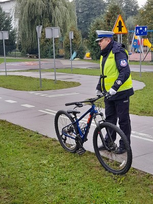 Umundurowany policjant w kamizelce odblaskowej, trzyma rower.
