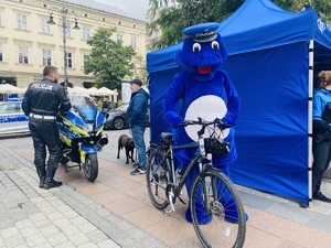 policjant przy motocyklu służbowym rozmawia z mężczyzną obok maskotka policji stoi przy rowerze.jpg