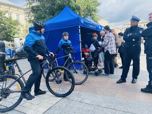 policyjny patrol rowerowy oraz policjanci z ruchu drogowego i mieszkańcy przy stoisku profilaktycznym.jpg