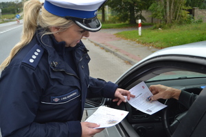 Policjanta ruchu dorgowego wręcza kierowcy ulotkę promującą WIZJĘ ZERO - dążenie do zerowej śmiertelności na drogach