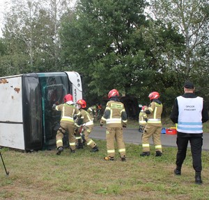 strażacy wycinający szybę w przewróconym na bok autobusie