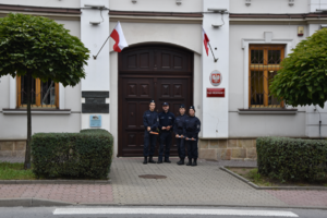 Policjant oraz uczniowie klasy policyjnej z elementami odblaskowymi na tle budynku Sądu Rejonowego oraz dwóch flag Rzeczypospolitej Polskiej.