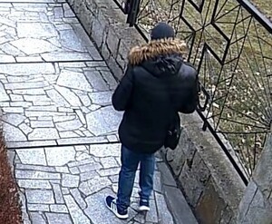 Zdjęcie z nagrania monitoringu. Widać stojącego tyłem mężczyznę. Ubrany jest w czarną kurtkę z kapturem obszytym brązowym futrem niebieskie dżins