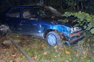 Samochód koloru niebieskiego z rozbitą szyba przednią i uszkodzonymi elementami karoserii stoi w rowie