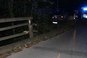 Samochód stoi w rowie, obok na drodze stoi radiowóz z włączonymi światłami błyskowymi, z boku widoczna uszkodzona drewniana poręcz mostu