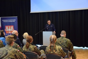 Policjant z Komendy wojewódzkiej Policji w Krakowie prowadzi prelekcję dla uczestników wystawy