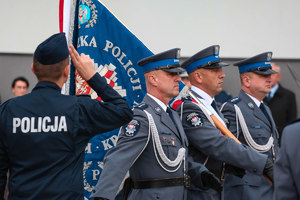 Policjanci idący ze sztandarem na pierwszym planie policjant salutuje do sztadaru