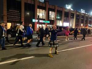 Grupa kibiców zmierza ulicą w kierunku stadiony, na pierwszym planie uśmiechnięty kibic ubrany w szkocki strój