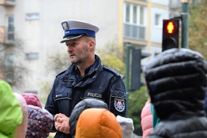 Policjant ruchu drogowego prowadzący prelekcję. w tle sygnalizator świetlny dla pieszych