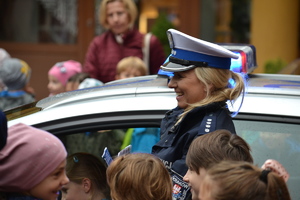 Policjantka ruchu drogoweg prowadzi prelekcję stojąc przy radiowozie. W tle otaczające ją dzieci