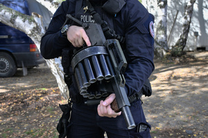 policjant trzyma ręczną wyrzutnię granatów łzawiących
