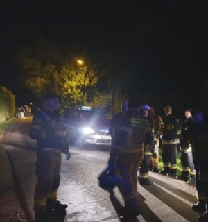 grupa strażaków podczas nocnych poszukiwań stojąca na drodze, w tle policyjny radiowóz
