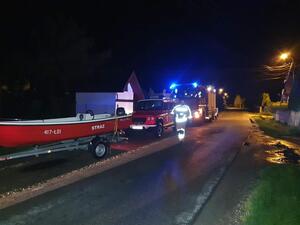 wozy strażackie i łódź motorowa stojące przy drodze, drogą idący strażąk