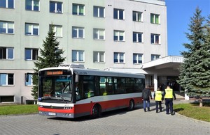 przed budynkiem oddziału stoi zaparkowany autobus miejski, obok policjanci w kamizelkach odblaskowych